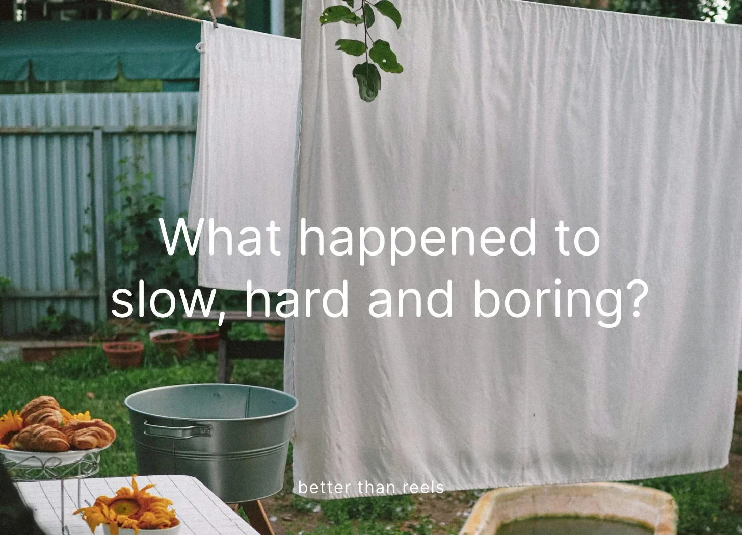 White sheets drying on a washing line in a green garden, with a metal tub and a bowl of pastries on a table.