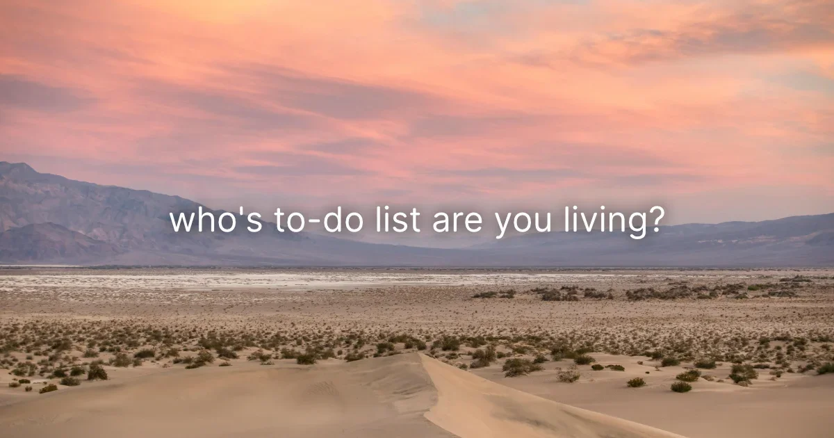 Sand dunes and distant mountains under a pink sunset sky, with the words “who’s to-do list are you living?”